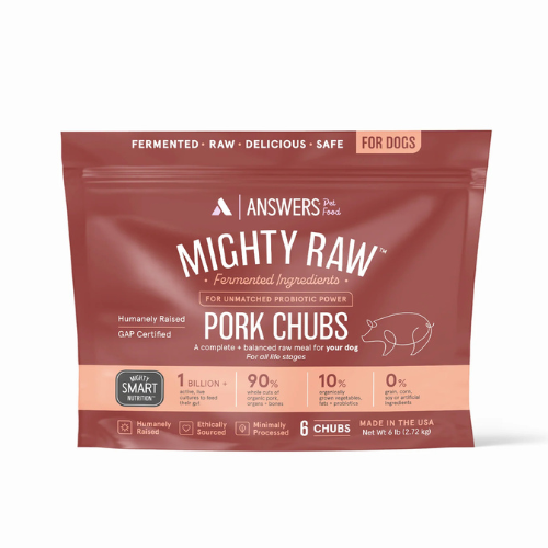 Front view of a red package of Answers Pet Food “Mighty Raw” fermented raw pork chubs for dogs. The packaging highlights fermented ingredients, probiotic power, humanely raised pork, minimal processing, and U.S. production. The bag contains six raw pork chubs with a net weight of six pounds and features icons indicating smart nutrition, ethical sourcing, and suitability for all life stages.