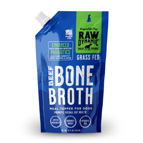 Blue and green spouted pouch of Raw Dynamic dog bone broth labeled “Beef Bone Broth.” The package has a white twist cap at the top corner and a green panel with the Raw Dynamic logo. Text reads “Enhanced with species-specific probiotics,” “Grass fed,” and “Meal topper for dogs promotes overall gut health.” Icons indicate “Limited ingredients,” “Humanely raised,” and “Antibiotic free.” Net weight is 12 fl oz (355 mL).