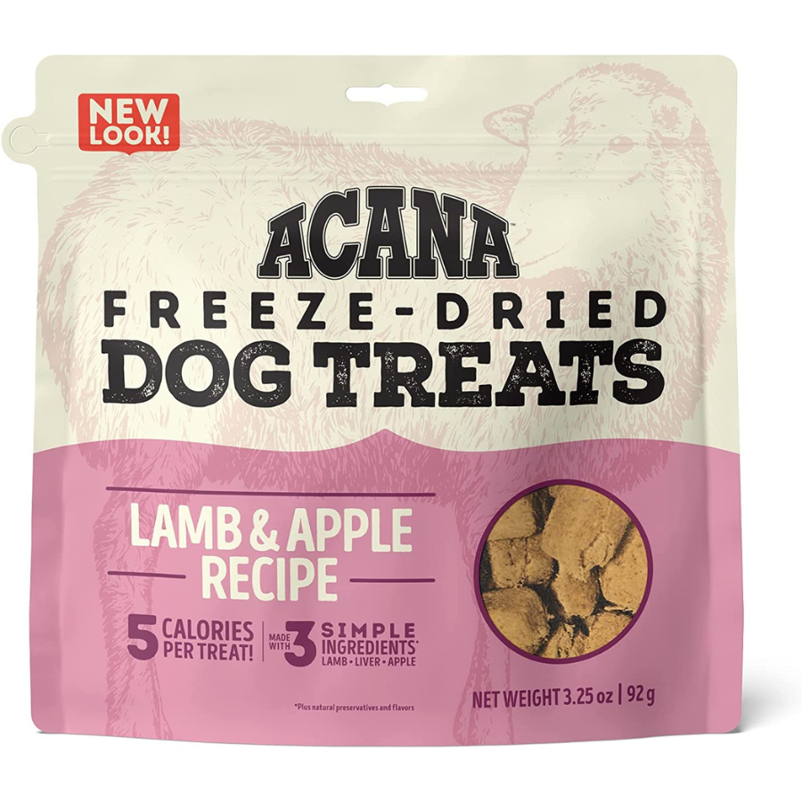 The front of the Acana Freeze-Dried Dog Treats bag, featuring a "Lamb & Apple Recipe." The bag is cream-colored on top with a pink bottom section. It includes a red "NEW LOOK!" banner and a small circular window at the bottom right revealing the actual brown, disk-shaped freeze-dried treats inside. The net weight is listed as 3.25 oz (92 g).