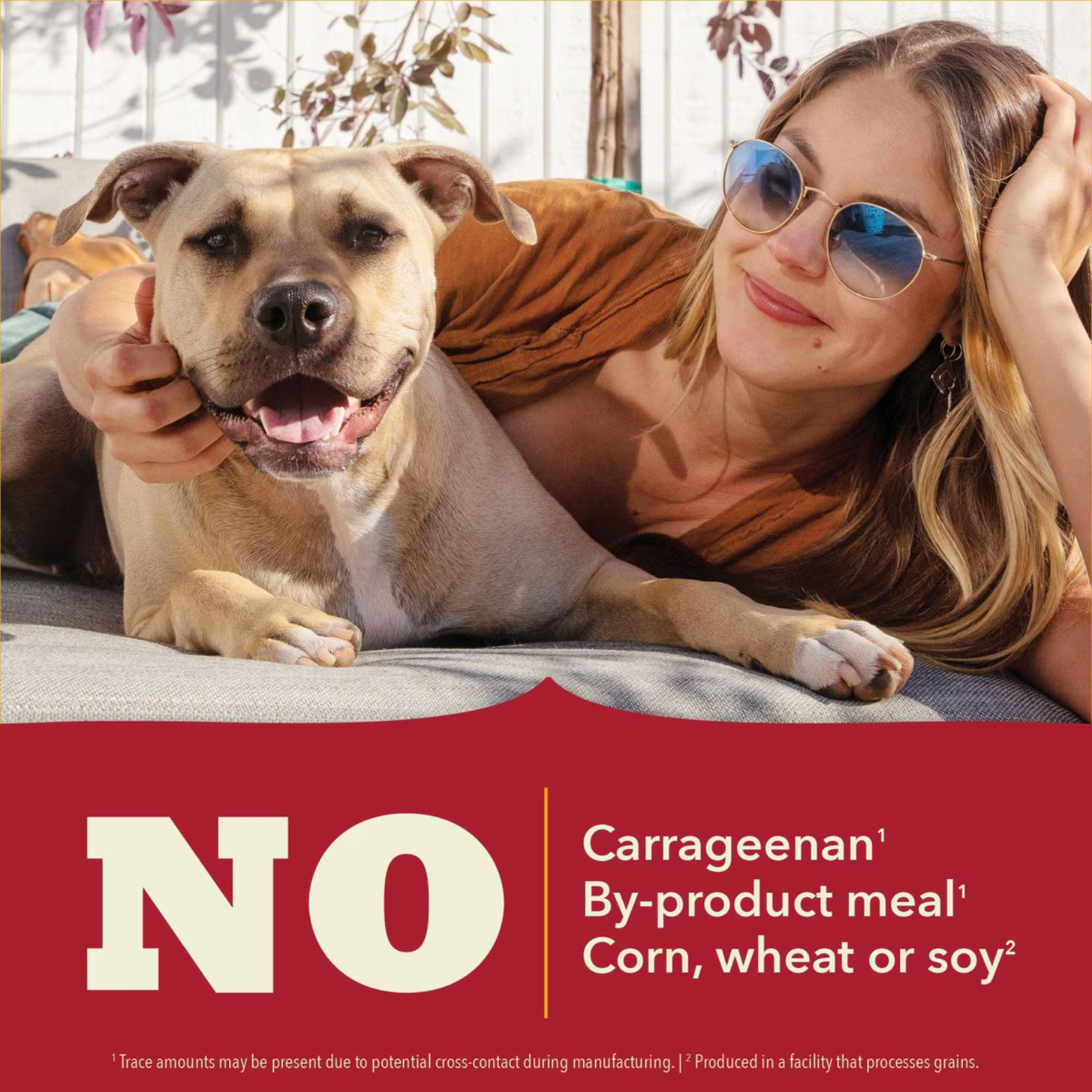 Photo of a smiling dog lying next to a person outdoors above text stating “No carrageenan, by-product meal, corn, wheat or soy.”