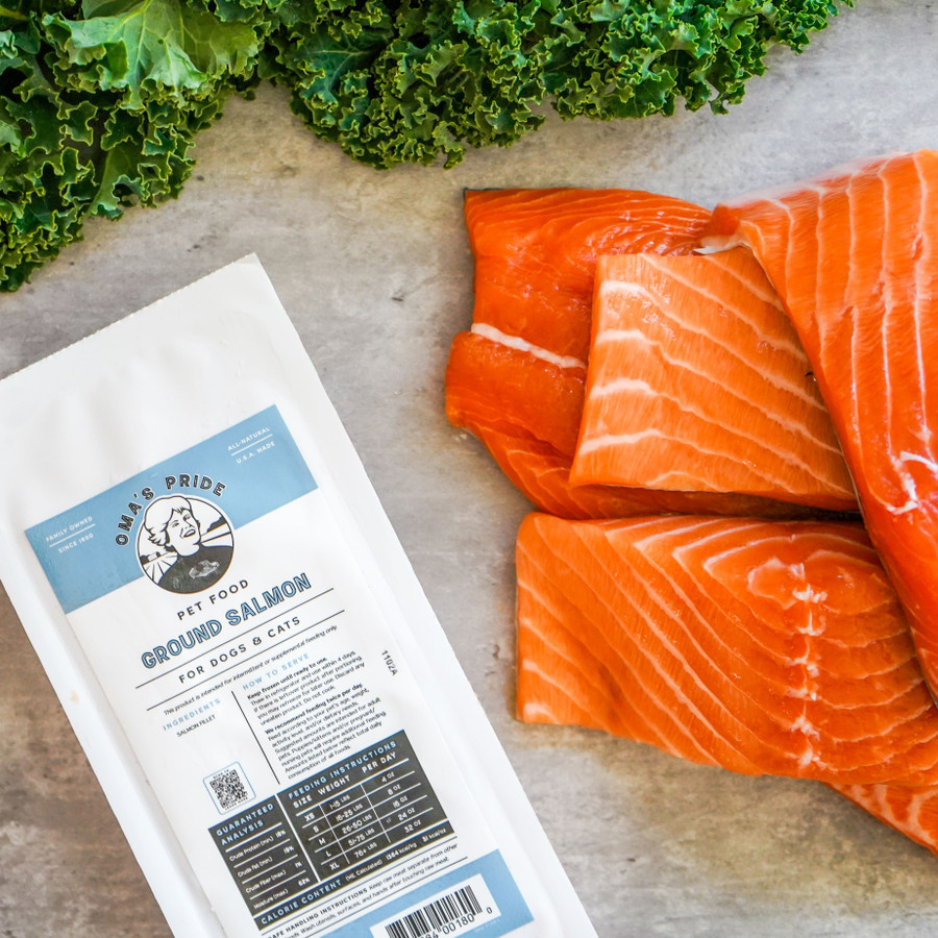 Raw salmon fillets arranged on a countertop beside the Ground Salmon package, with leafy greens visible at the top of the frame.