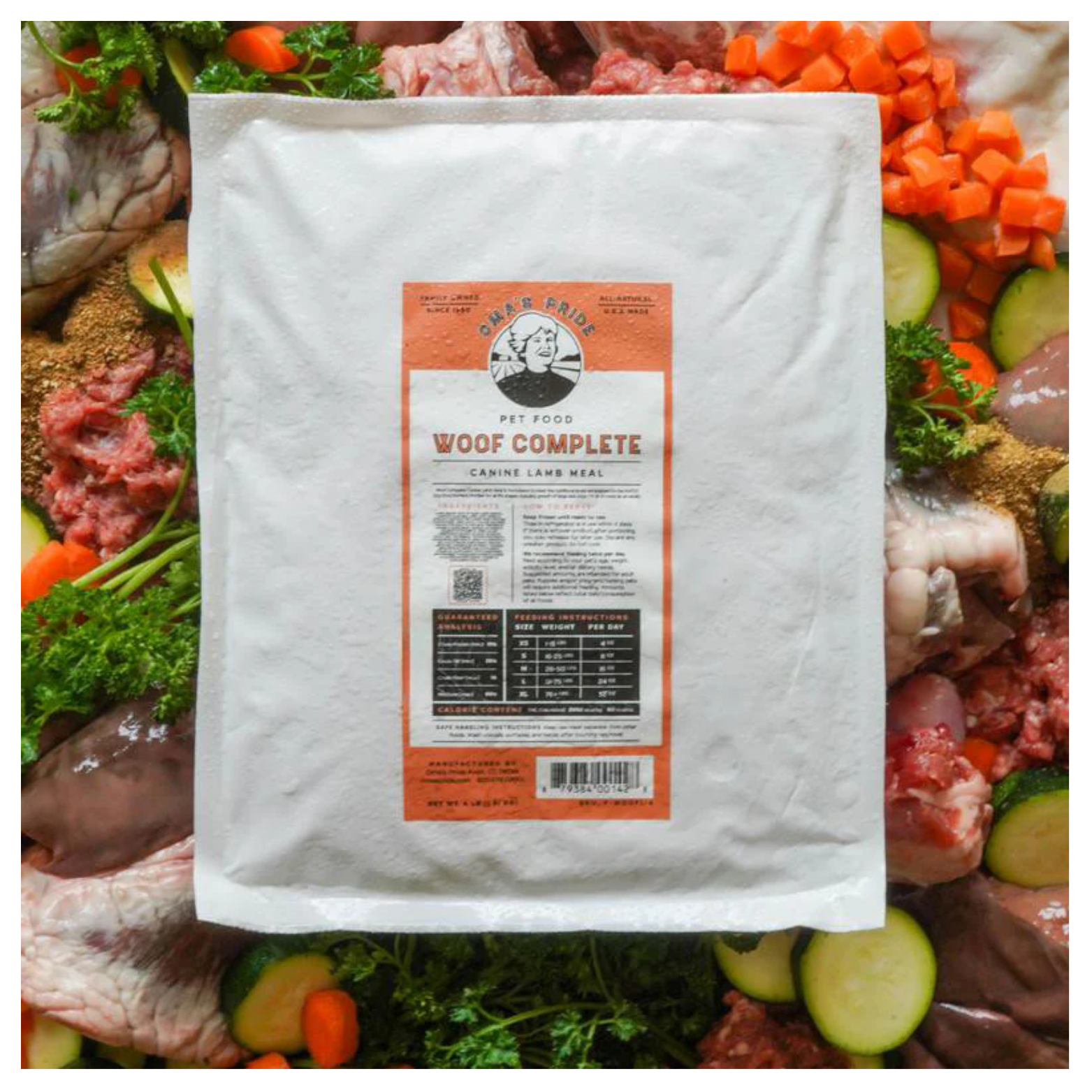 A frozen package of Oma’s Pride Woof Complete Canine Lamb Recipe placed on top of raw lamb ingredients and vegetables.