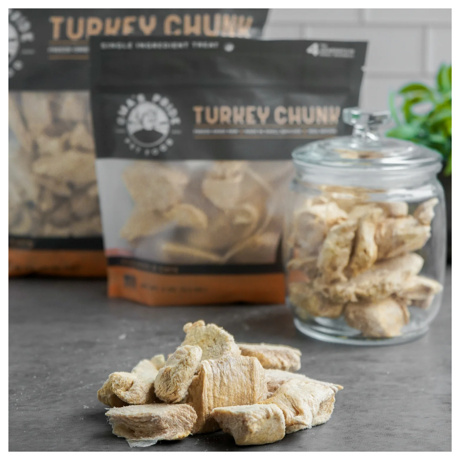 Freeze-dried turkey chunks arranged on a countertop in front of Oma’s Pride packaging and a glass jar filled with treats, with the background softly blurred.