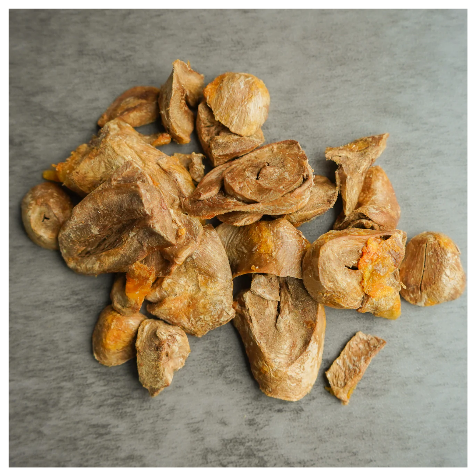 A pile of sliced freeze-dried turkey heart treats with a brown and orange texture resting on a gray surface.