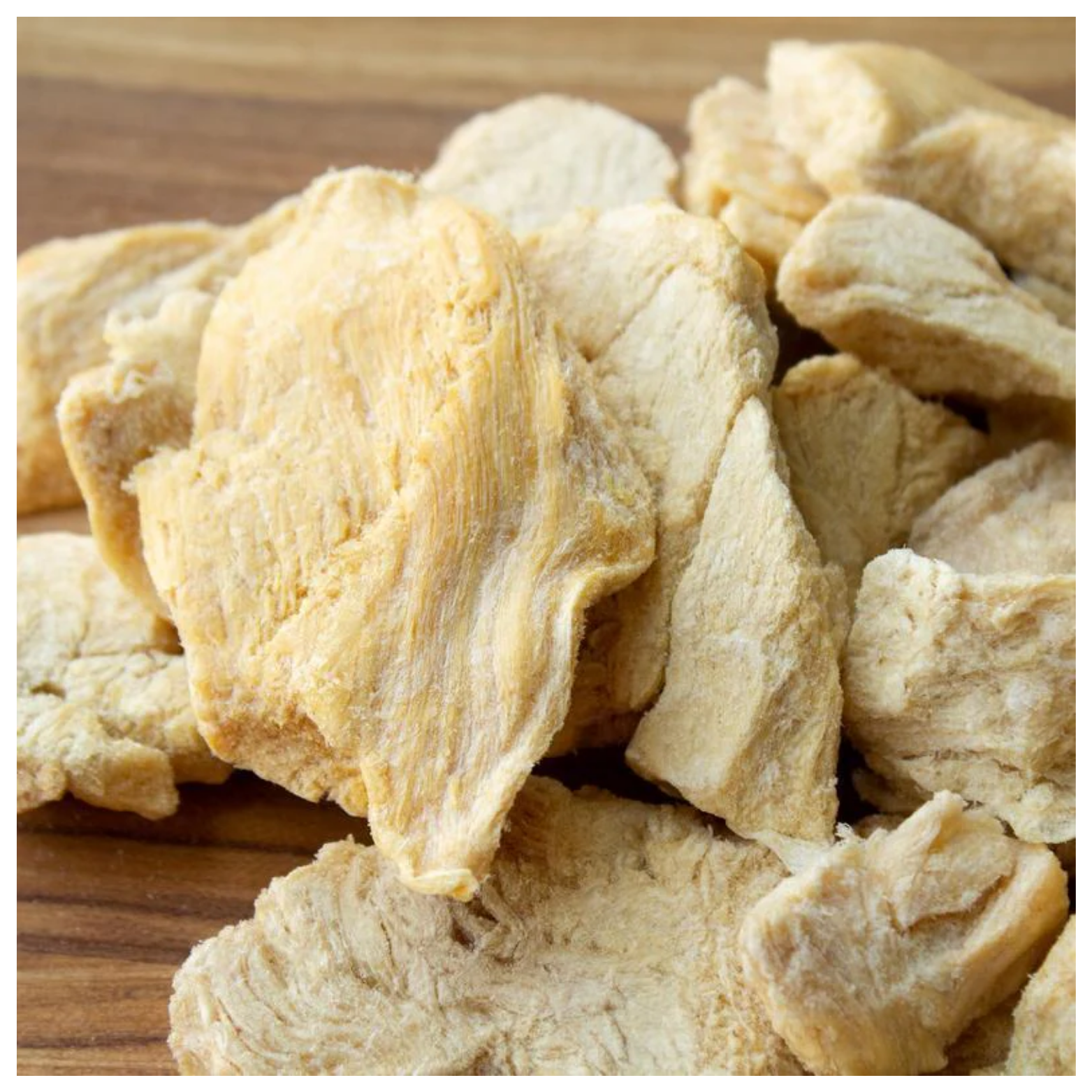 Close-up view of several freeze-dried chicken chunks with a light, porous texture resting on a wooden surface.