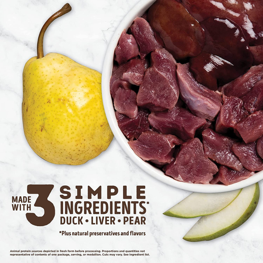 A simple ingredient display featuring a whole yellow pear, a white bowl filled with raw duck and liver pieces, and two pear slices on a marble surface. The text reads "Made with 3 Simple Ingredients: Duck, Liver, Pear."