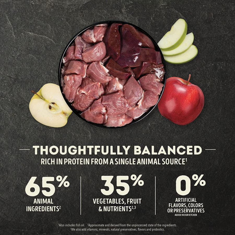Overhead view of a black bowl filled with raw lamb meat and lamb liver, surrounded by whole and sliced apples on a dark surface. Text emphasizes a thoughtfully balanced recipe with protein from a single animal source.